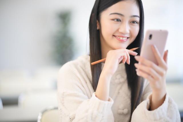 スマホを見ながら 鉛筆をもって勉強する女性